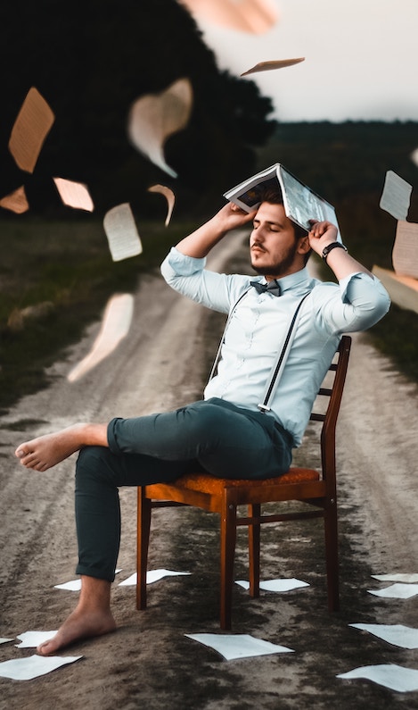 Great storytelling: image of a young man sitting on a chair in a road while sheets of paper rain down on him