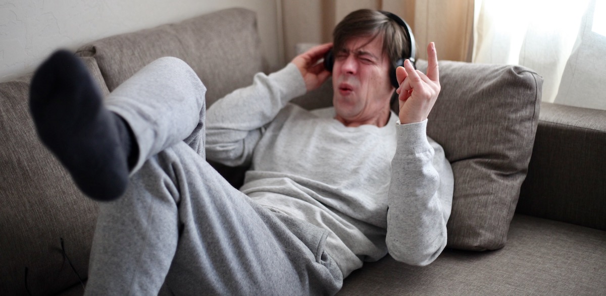 Critical listening: man lying on a couch with headphones on pulling a face